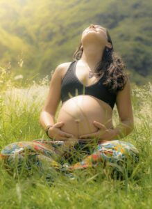 une femme enceinte assise dans l'herbe caresse son ventre