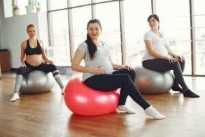 Des femmes enceintes calmes, assises sur des ballons de gymnastique, pendant un entraînement prénatal dans une salle de sport spacieuse et lumineuse, en journée, tout en se souciant de leur santé.