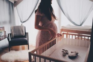 femme enceinte en robe blanche sans manches en dentelle debout à côté d'un berceau en bois brun