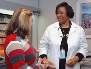 femme noire docteur en blouse blanche avec un stéthoscope et une femme enceinte avec un pull multicolore